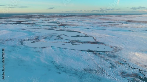 Drone aerial shot showing the icy waters and snow-covered shores of Guba Malaya Volkovaya bay in the harsh Barents Sea environment.