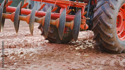 Close-up of a tractor's tiller on textured soil, highlighting agricultural machinery in action.
