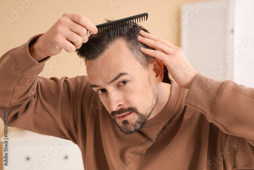 Handsome man with hair loss problem combing in bathroom, closeup