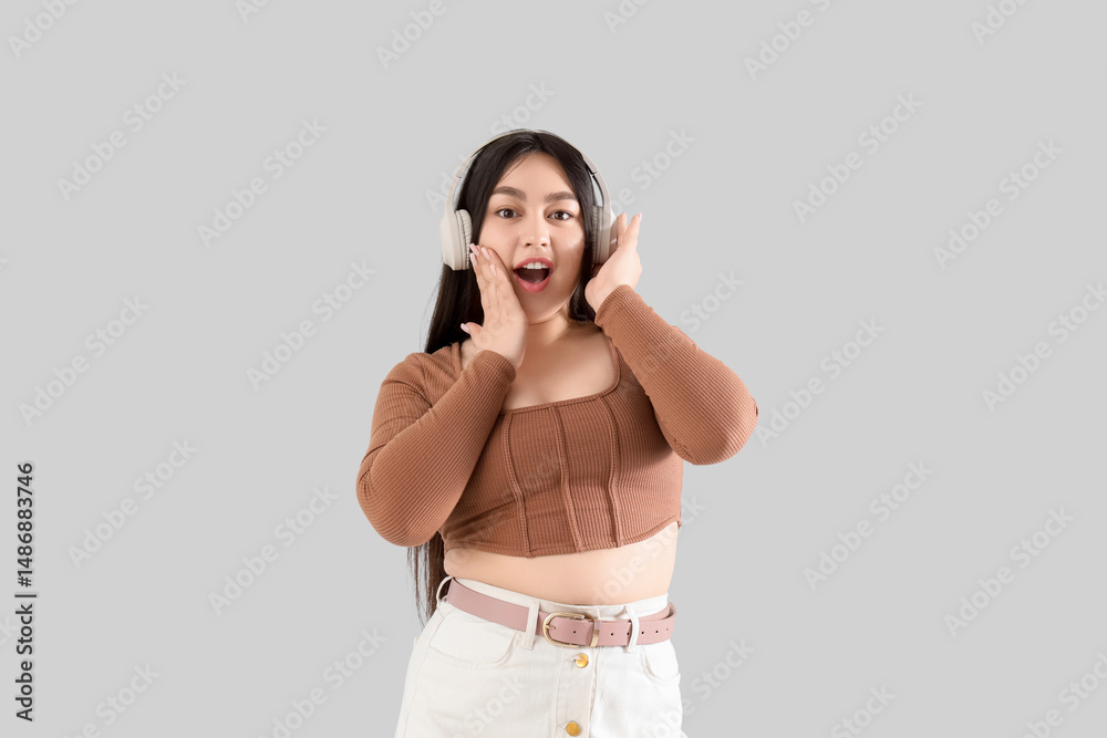 Naklejka premium Surprised young woman in headphones on light background