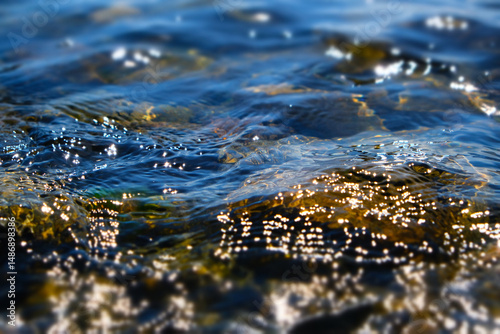 Cristal river, waterfall glowing water background, stones, rapids and boulders. Texture clear cold sea water with reflection sunlight. Falling and flowing water. Scenery lake. Shallow DOF