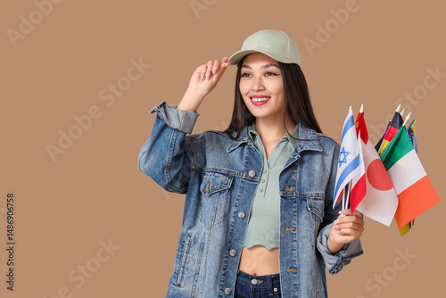 Young Asian girl with flags of different countries on beige background