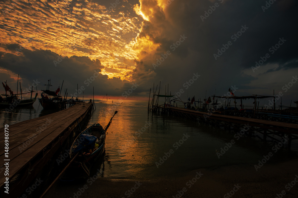 Fototapeta premium Background of golden sunlight in the morning by the sea, with fishing boats moored at the pier, waiting for the time to go out to fish again.