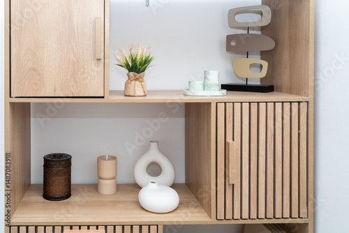 A wooden shelf showcases a collection of decorative items, including vases and a candle, set against a minimalist wall. This cozy arrangement enhances modern interior decor.
