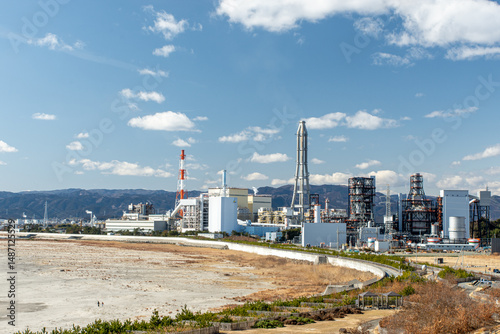 Iwama Beach, Iwaki City, Fukushima, Japan – winter sandy shoreline facing an industrial complex with power-plant chimneys and refinery towers beside the blue Pacific Ocean under a clear sunny sky
 photo