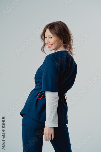 Young beautiful woman doctor standing with back in blue clothing on a white background, with copy space to the side.