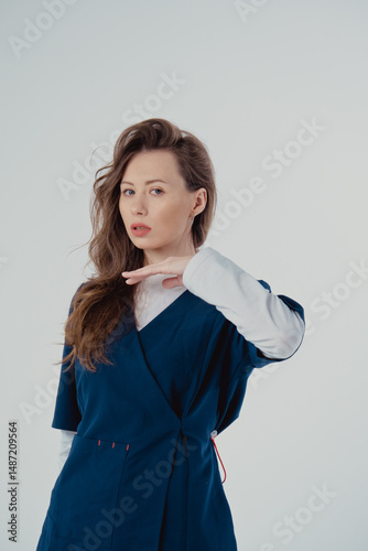 Young beautiful woman doctor in blue clothing on a white background, with copy space to the side.
