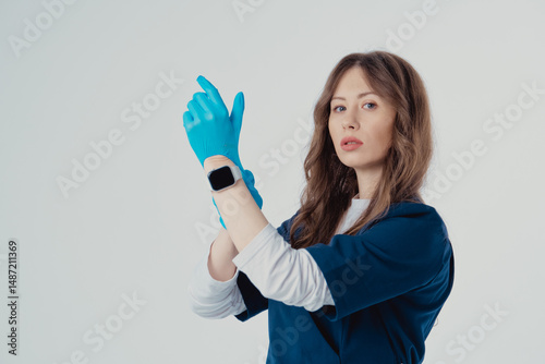 Photo of beautiful doctor in protective mask putting on medical gloves against white background.