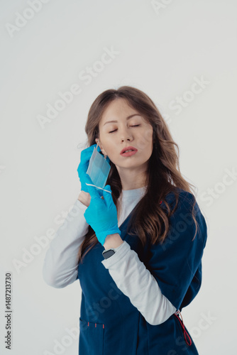 Doctor in protective mask putting on medical gloves against white background