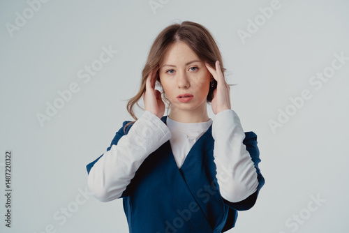 Portrait of a cardiologist girl in a blue uniform with her hands near her face on a white background, with copy space to the side.