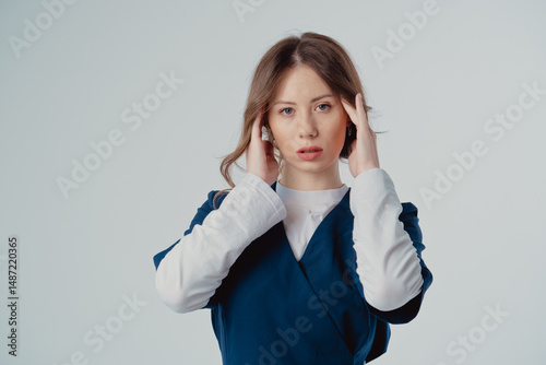 Portrait of a cardiologist girl in a blue uniform with her hands near her face on a white background, with copy space to the side.