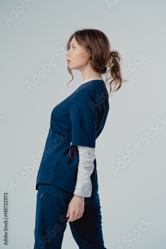 Young beautiful woman doctor in blue clothing on a white background, with copy space to the side.