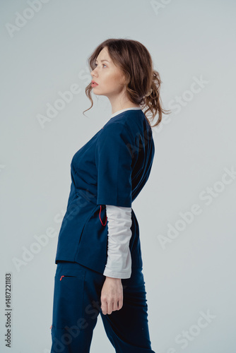 Young beautiful woman doctor in blue clothing on a white background, with copy space to the side.