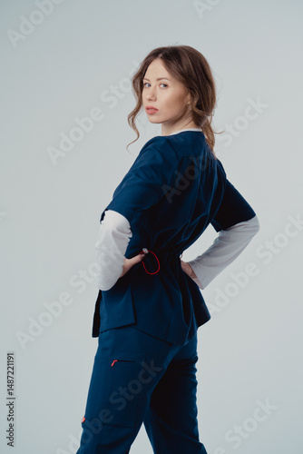 Young beautiful woman doctor in blue clothing on a white background, with copy space to the side.