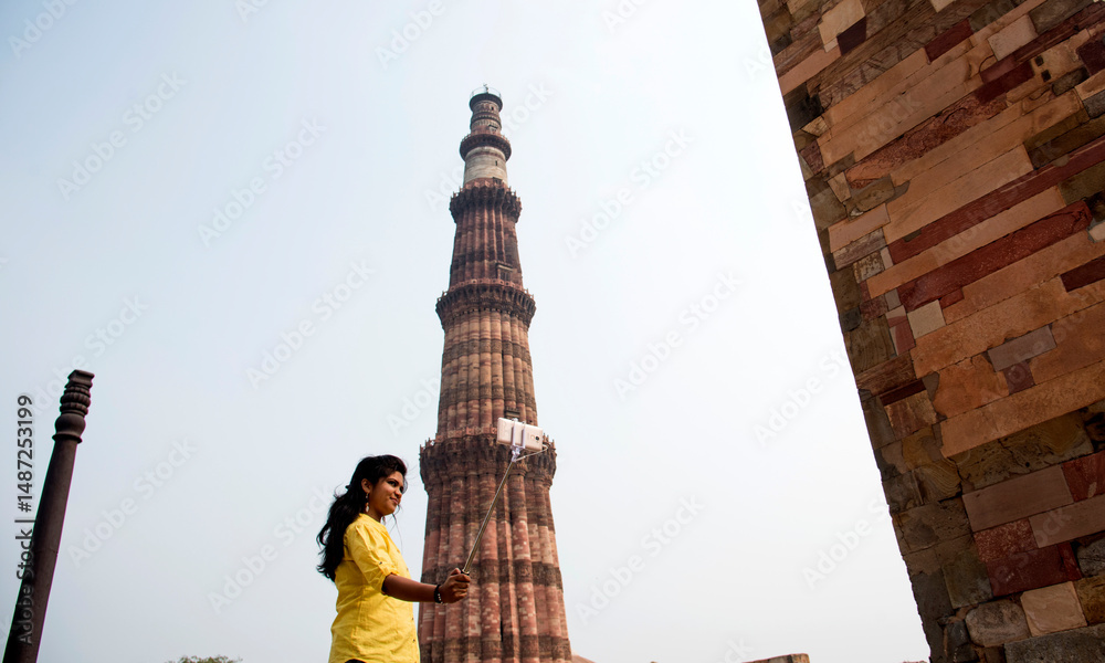 Fototapeta premium Tourist woman taking selfie in front of Qutub Minar, Delhi, India.