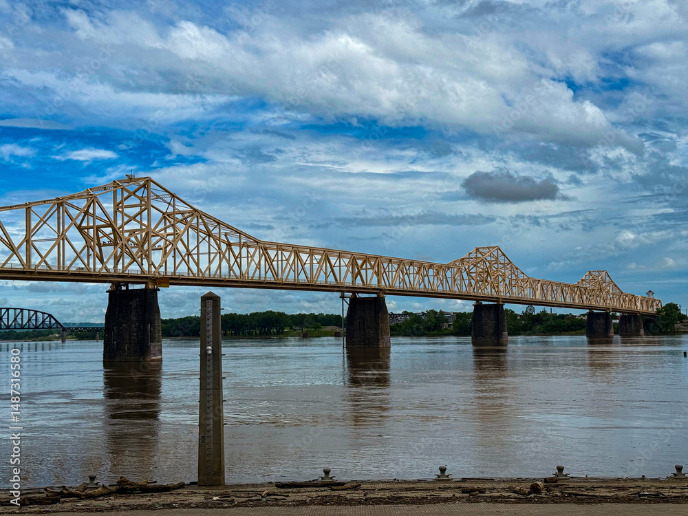 Fototapeta premium Yellow Truss Bridge Spanning a River Under a Cloudy Blue Sky
