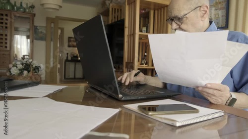 Man Reviewing Documents While Using Laptop at Home Office. Dolly