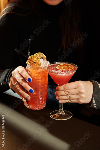 Woman holding two fancy cocktails with orange garnish in a tiki mug and martini glass