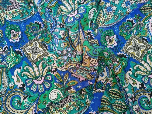 Paisley patterned fabric detail swirled background, featuring curved, teardrop shaped motifs of Persian origin with vibrant colors like blue and green, texture, top view