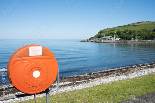 Bright orange lifebuoy case, essential water safety rescue equipment beside calm ocean, bright sunny day seaside