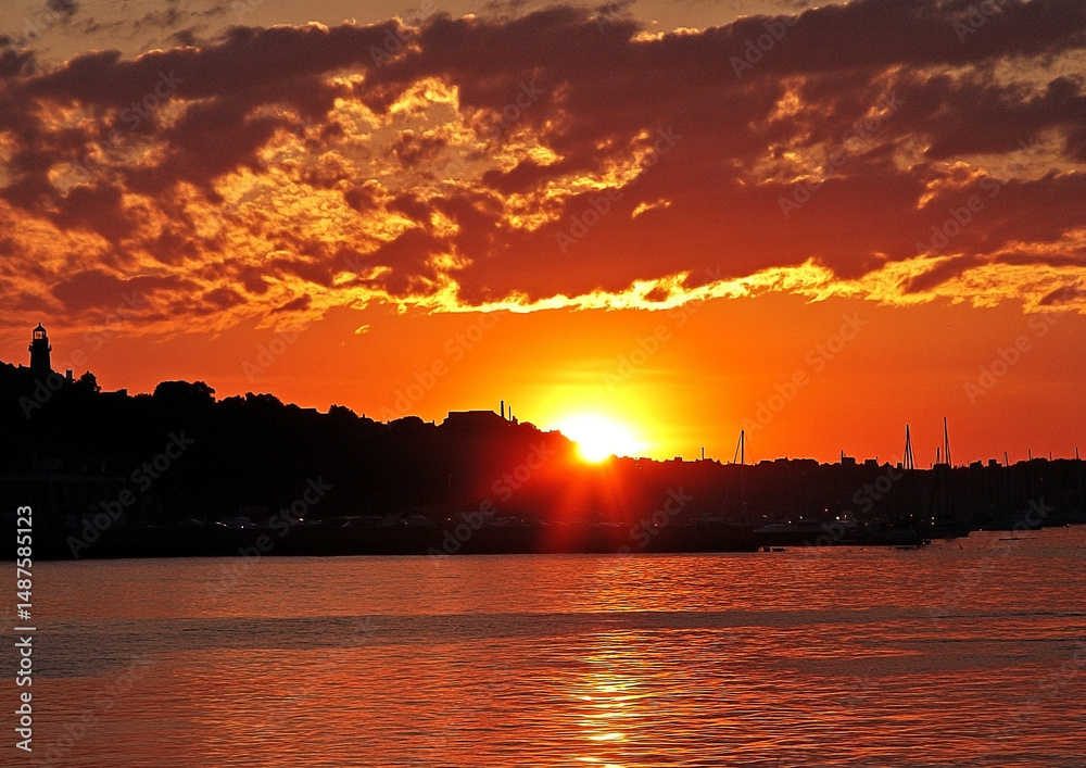 Naklejka premium Golden coastal sunset view with silhouetted shoreline and vibrant skies