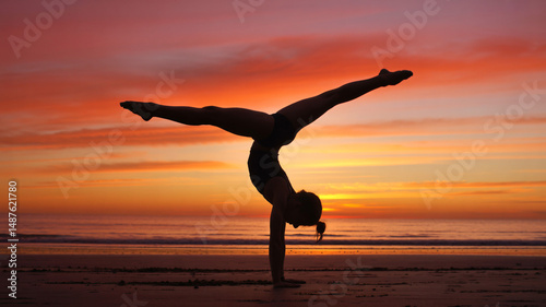 Gymnast in handstand silhouette against a fiery sunset