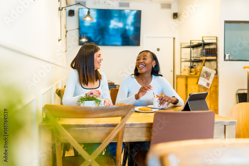 Two young women laughing and talking at coffee shop table
