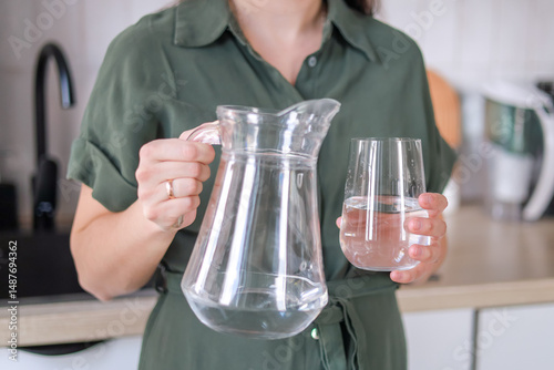 woman holding a pitcher in a glass with water in the kitchen water helps to increase hydration levels and improve metabolism concept of healthy lifestyle, cooking blogs.