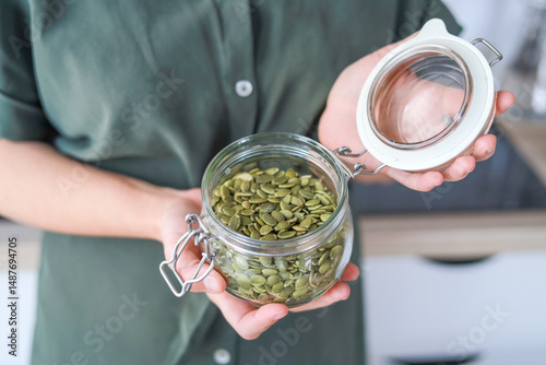 Woman's hands holding green pumpkin seeds in a glass jar in the kitchen, they are good for skin and hair due to vitamin E concept of wellness, nutrition.
