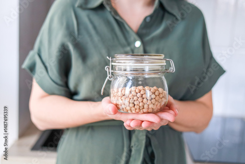 A woman holds a glass jar of chickpeas this product is rich in protein and fiber to maintain health. The concept is healthy eating, cooking.