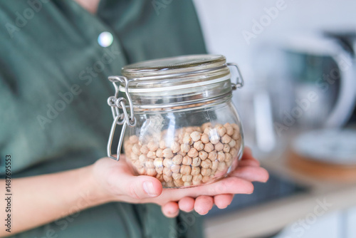 A woman shows chickpeas in a glass jar they are an excellent source of plant-based protein and healthy fats for health. The concept is wellness, organic products.