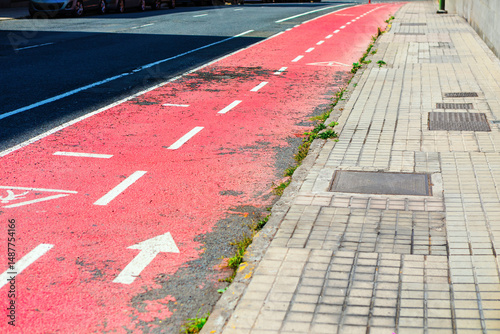 Bike lane showing signs of weathering, contrasts with gray sidewalk, a common urban scene. City street scene with faded pink bike lane and white markings, borders sidewalk of light gray paving stones photo