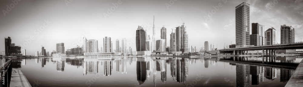 Fototapeta premium Monochrome city skyline with tall skyscrapers reflecting on calm water under a cloudy sky, Dubai Marina bay UAE