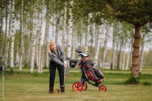 Female golfer hits the ground before the ball, causing a chunk of turf to fly — an unsuccessful shot during a swing on a wooded golf course..