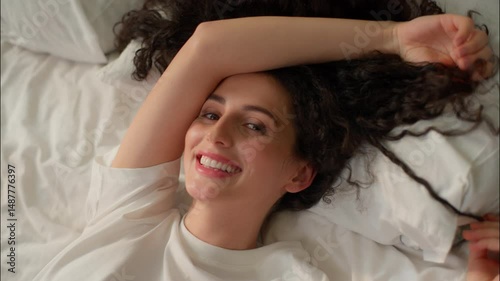 Caucasian happy woman curly girl relaxing in bed cozy home bedroom beautiful female pampering smile awake morning weekend in hotel apartment wake up soft mattress pillow health enjoy rest comfortable
