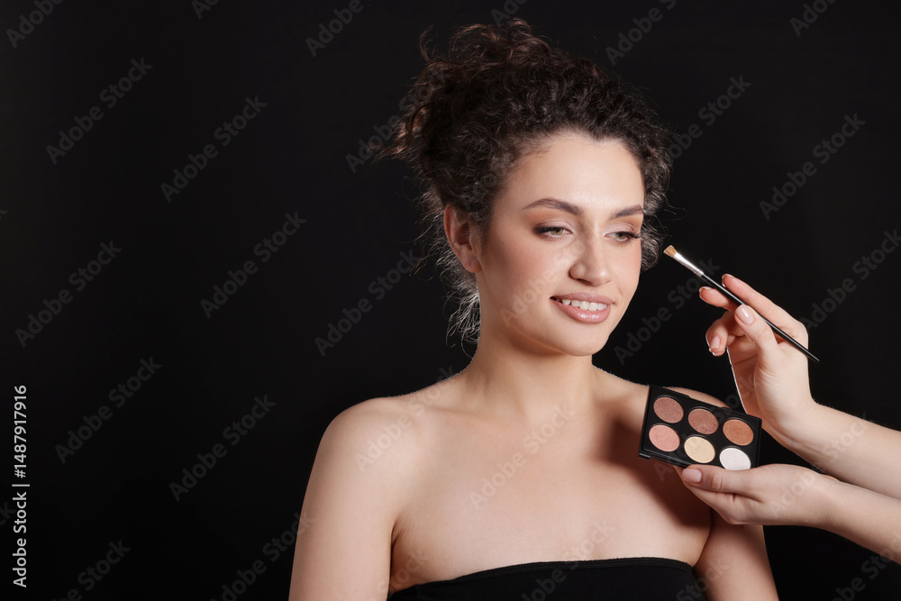 Obraz premium Makeup artist applying eyeshadows onto woman's face on black background, closeup. Space for text