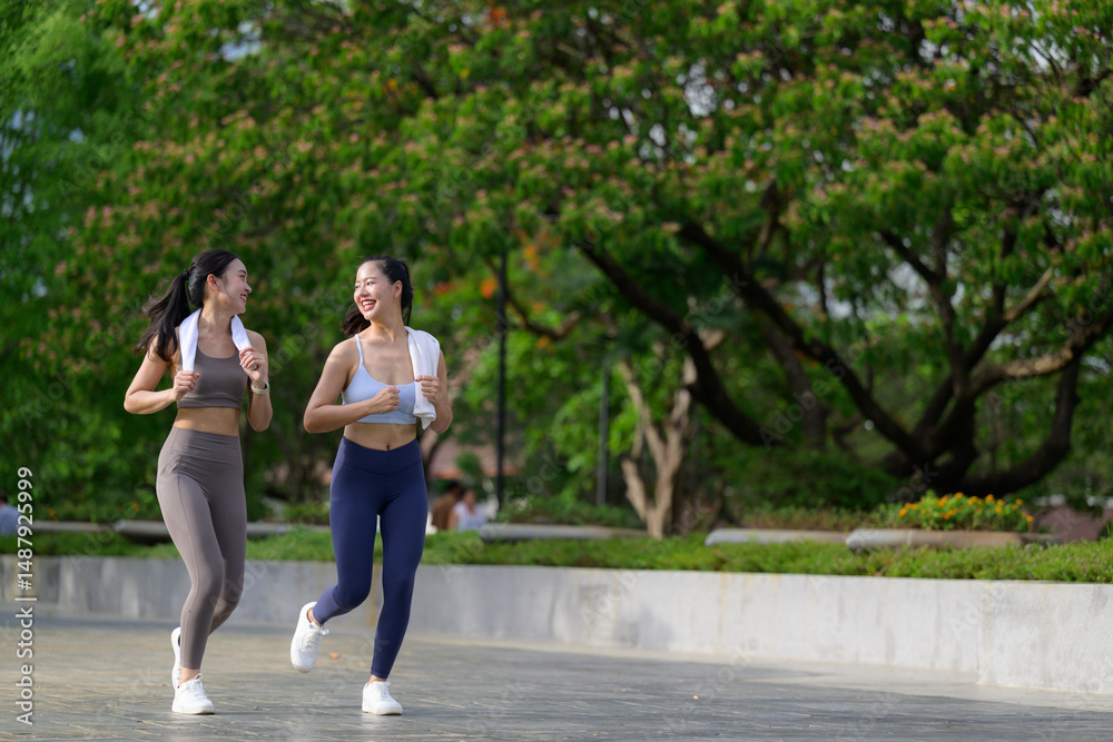 Obraz premium Two female athletes are jogging and chatting during their workout in a park