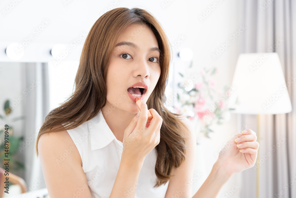 Young, woman, beauty, skincare, lipstick: Asian woman holds lip balm and smiles directly, gently touching mouth, proud of moisturized lips, healthy glow and playful morning cosmetic routine Young, woman, beauty, skincare, lipstick: Asian woman holds lip balm and smiles directly, gently touching mouth, proud of moisturized lips, healthy glow and playful morning cosmetic routine