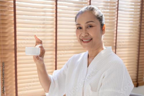 Fotografi senior, woman, skincare, beauty, cream: Asian senior woman in white robe holds m