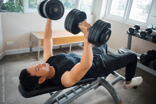 Asian man performing incline bench press with dumbbells