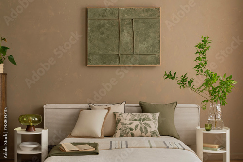 A serene bedroom with beige walls and a green-toned abstract mock up poster above a neatly made bed with neutral and botanical-themed cushions. Home decor.