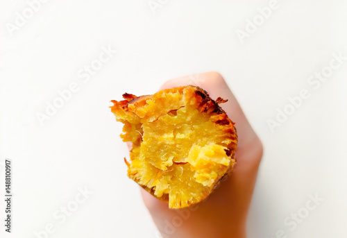 Hand holding a roasted honey sweet potato on white background