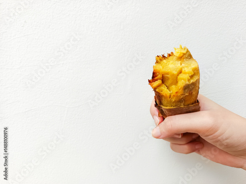 Hand holding a roasted honey sweet potato on white background