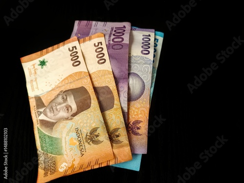 Close-up of Indonesian Rupiah banknotes in various denominations (5000, 10000, 50000) spread on black background