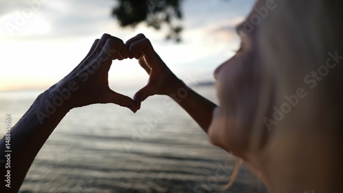 A happy, mature woman forms a heart shape with her hands, enjoying the serene atmosphere of the lake near Concepcion volcano during sunset in Nicaragua.