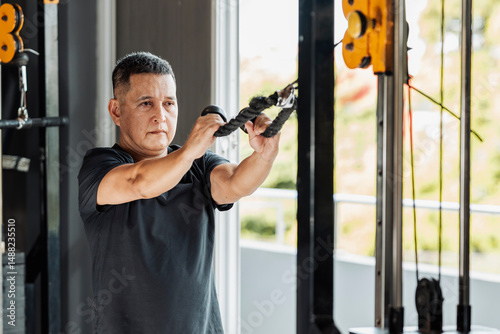 Photos Southeast Asian man in his 50s performing face pulls with a rope attachment at an open-air gym to target rear delts