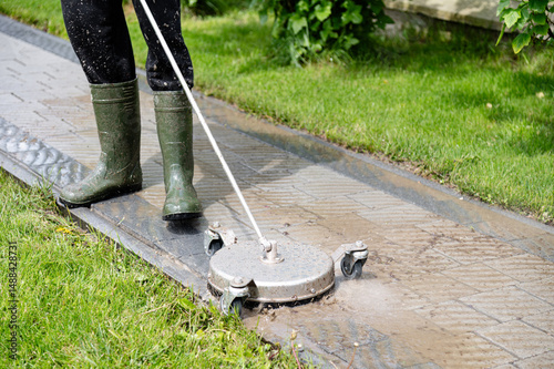 Professional paving stone cleaning. Person using a surface cleaner on a paved outdoor walkway during a sunny day in a residential area