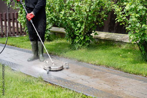 Power washing concrete walkways in a residential garden during a sunny afternoon for thorough cleaning and maintenance. Professional paving stone cleaning.