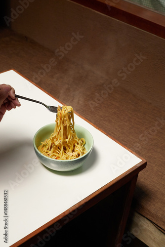 Steaming Bowl of Noodles Being Twirled With a Fork on a Wooden Table
