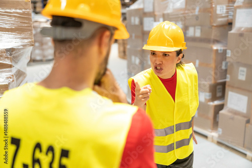 Angry female warehouse worker yelling at male colleague during conflict in the storage area.
